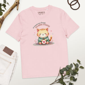 Roséfarbenes T-Shirt mit Katzenmotiv liegt flach auf einem hellen Untergrund. Das Motiv zeigt eine orangefarbene Katze mit einem Stickrahmen, darauf ein Herz. Um die Katze liegen bunte Fäden. Darüber steht der Text: ‚Ich brauche keine Therapie, ich kann sticken!‘ – Design von Vindalys. Daneben liegen eine helle Hose, grüne Blätter, ein Holzstück und ein Armband.
